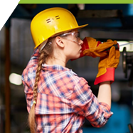 A middle school student wearing a hard hat, protective goggles and safety gear working in the carpentry shop. 