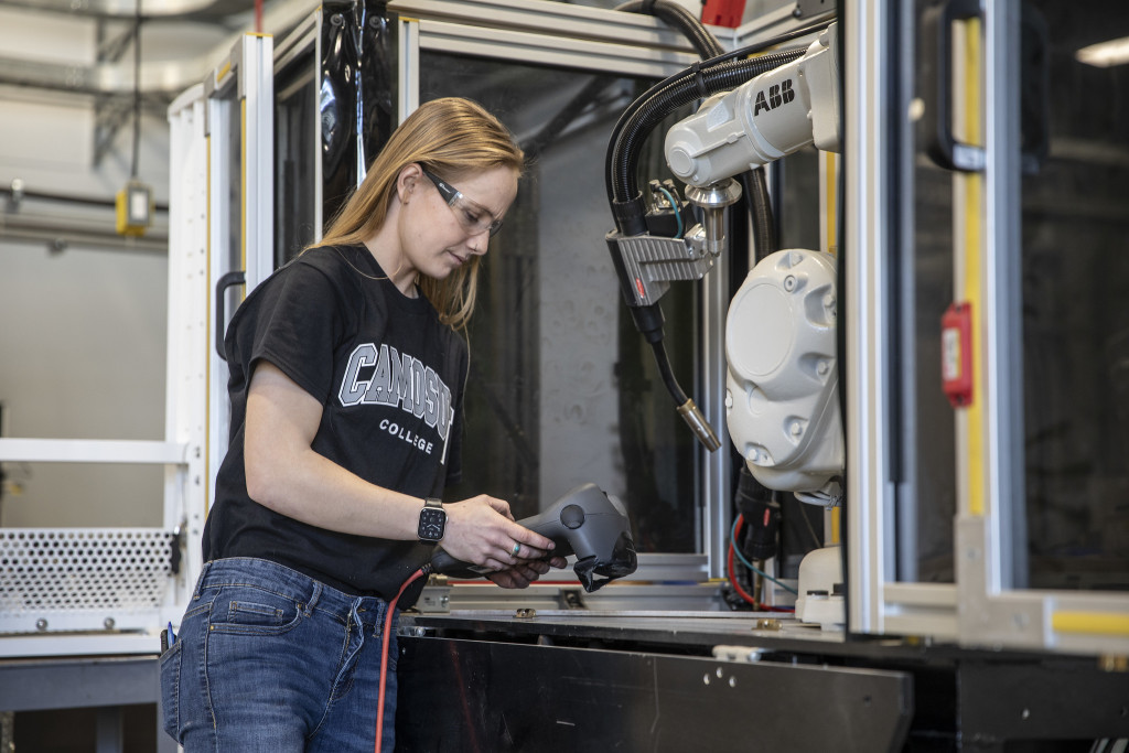 A woman wearing a black Camosun College t-shirt works on something in a technical environment.