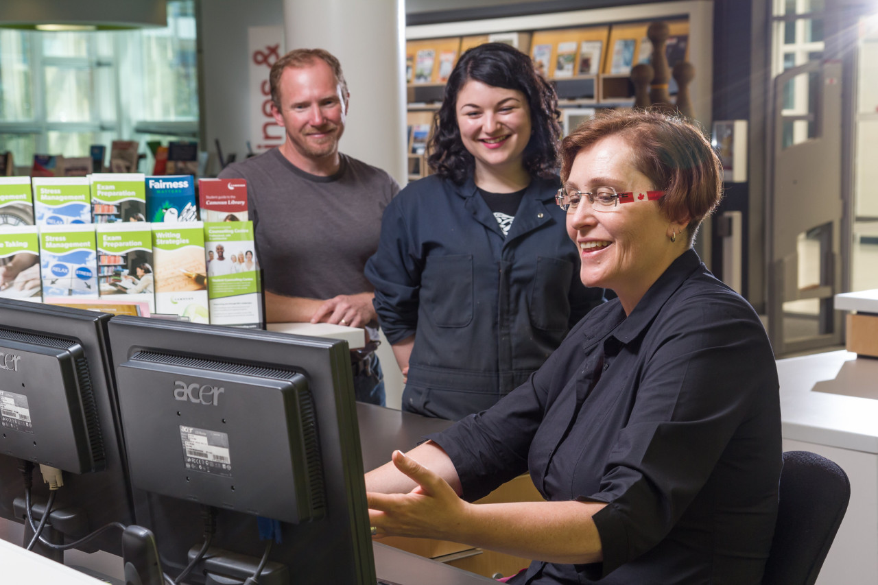 A staff member shows 2 people something on a computer