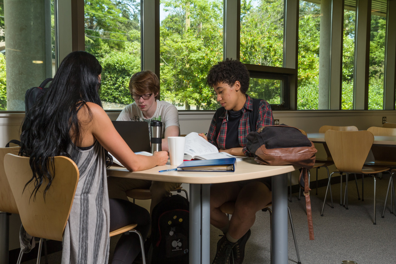 Three students look at books around a table in the library.