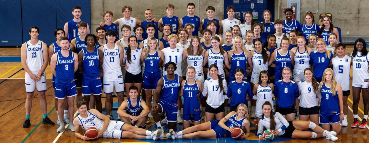 Group shot of the 2023 Camosun Chargers including both Women's and Men's Basketball and Volleyball Team Members. Photo takes place on the centre of home court in the PISE Building on Interurban campus.