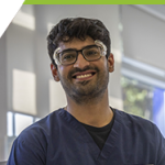 Ansh smiling towards the camera, wearing his safety glasses and rags at the Campus Dental Clinic.