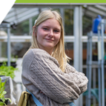 Kyla standing in the greenhouse, smiling