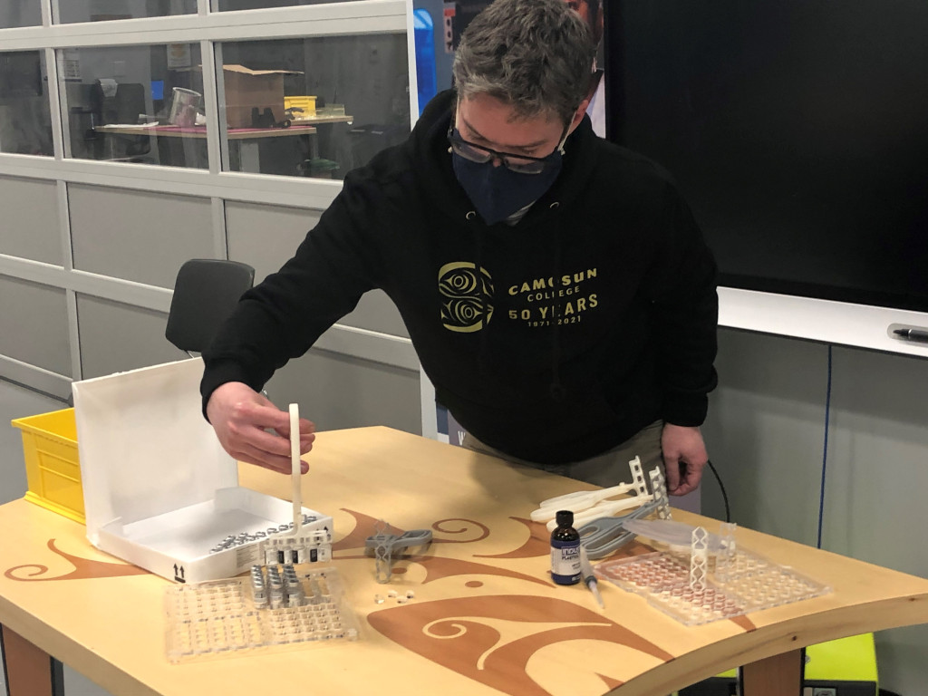 Man in black hoodie lifts vaccine vials onto an acrylic tray