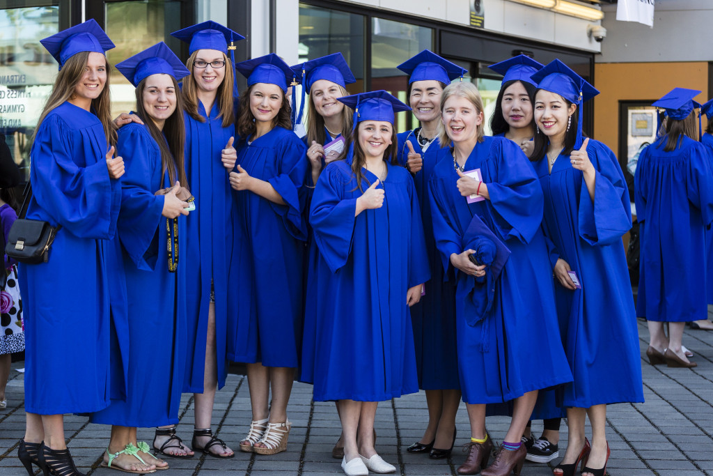 A group of students wearing blue graduation gowns and caps stand together in a group of a photograph