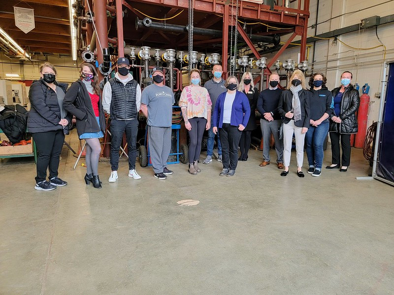 A group of people are gathered in a large trades training classroom and are all looking directly at the camera.