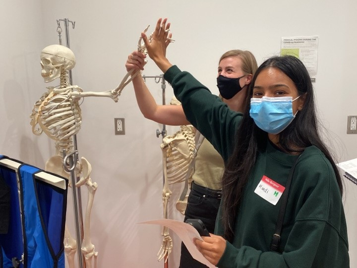 Two MRAD students high five a model skeleton used for training.