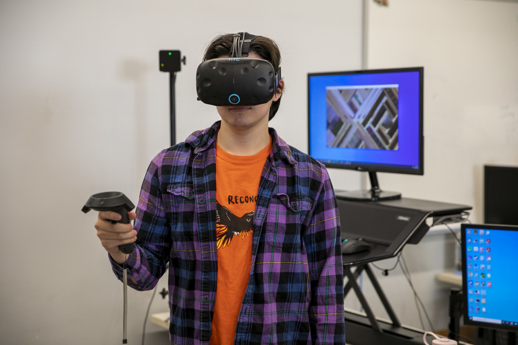 A man with a virtual reality headset stands in front of a computer. 