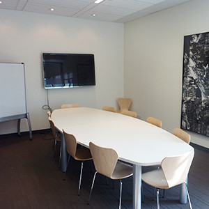 A meeting room with a boardroom table, large screen mounted on the wall and a flip chart.