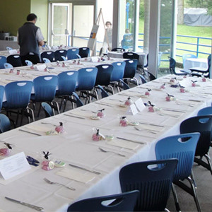 A large and bright dinning room. The tables are set with white table cloths and silverware. 