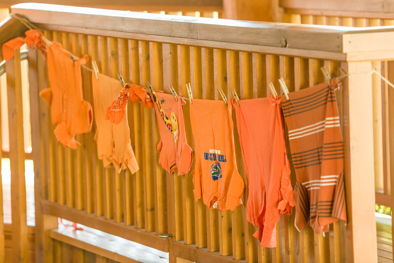 A row of childrens' orange t-shirts hang in a line against a wooden railing.