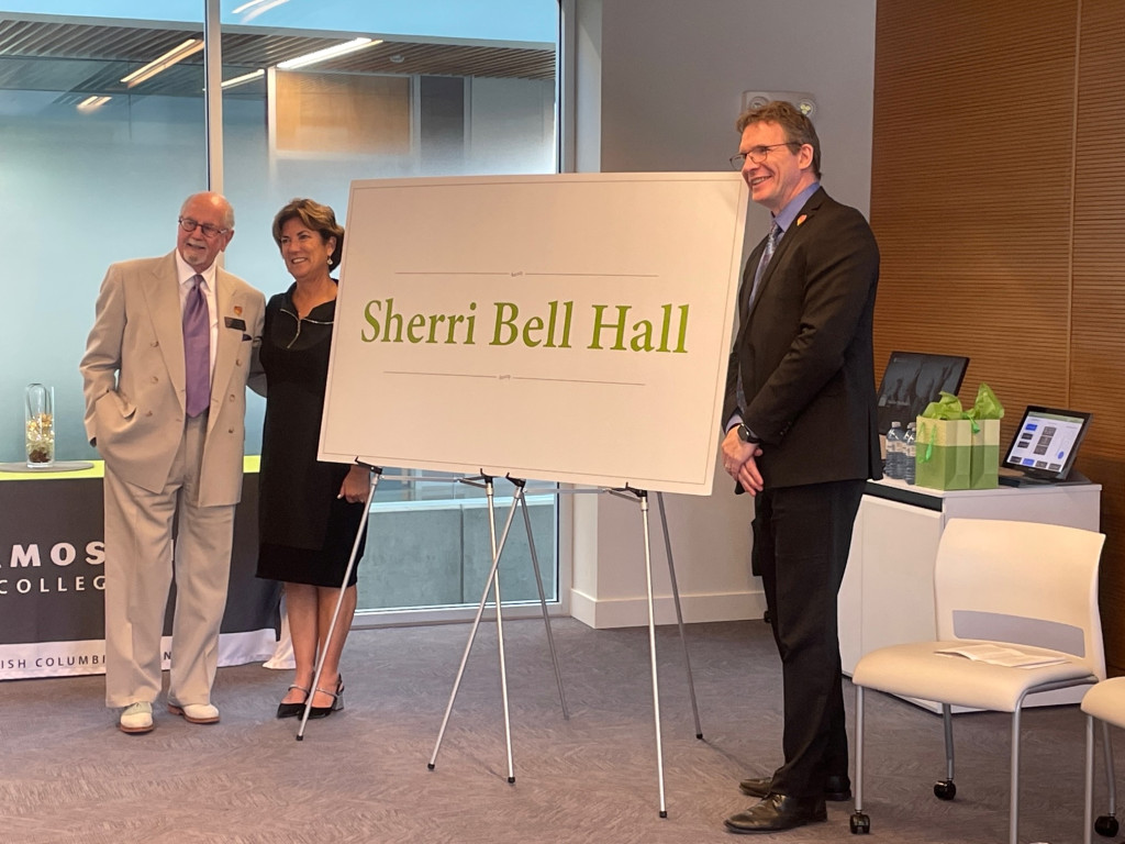 Board Chair Monty Bryant, retired president Sherri Bell and current president Lane Trotter stand next to a large sign indoors that states Sherri Bell Hall in large green letters