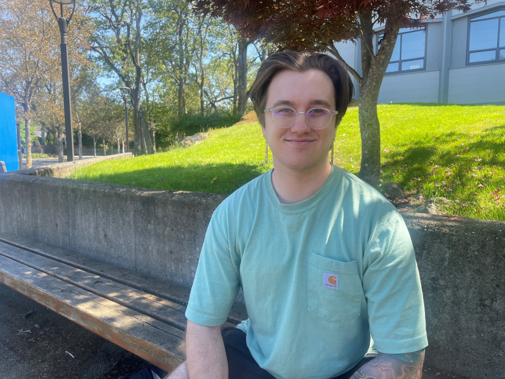 Photograph of a young male student wearing a green shirt sitting in the shade on a sunny day