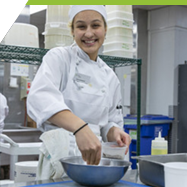 A culinary arts apprentice  preparing food in a professional, industrial kitchen. 