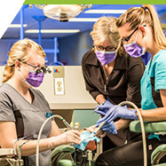two dental students and one instructor in clinic, using tools on a dental training manikin set up in the dental chair