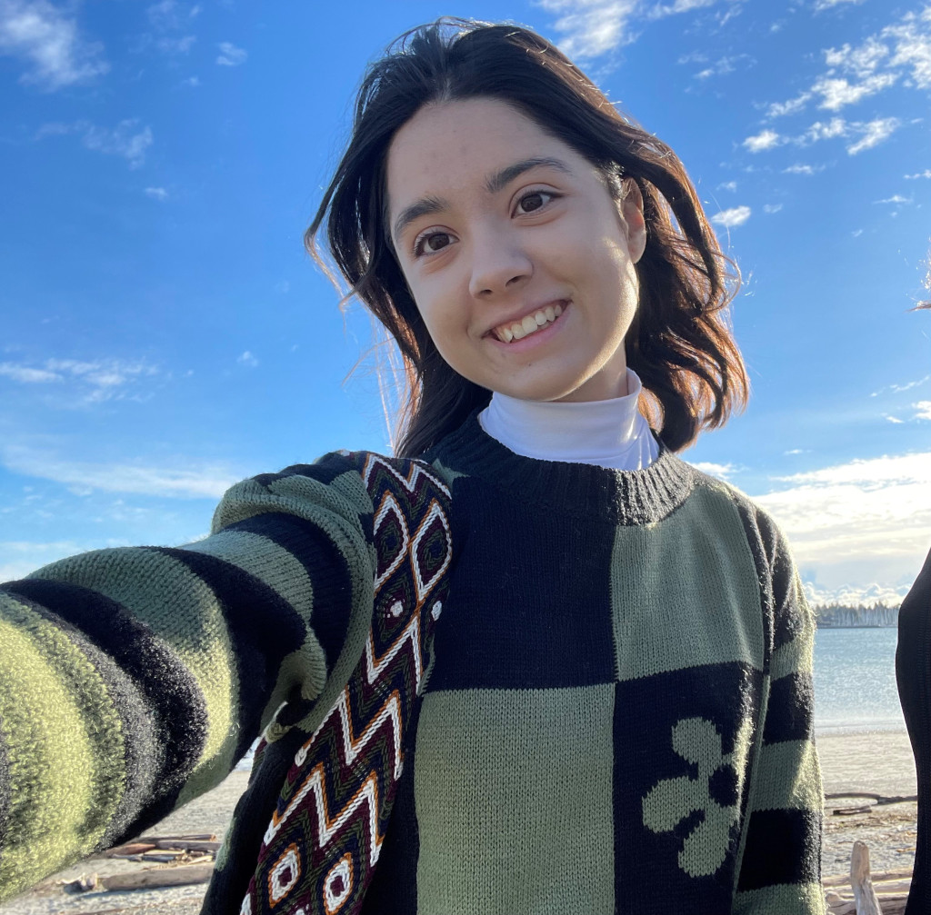 A young woman in a sweater stands in front of the blue sky on a beach