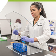 student looking at test tubes in lab wearing gloves and labcoat