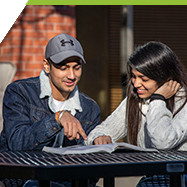 two students studying together outside library at picnic table in sunshine