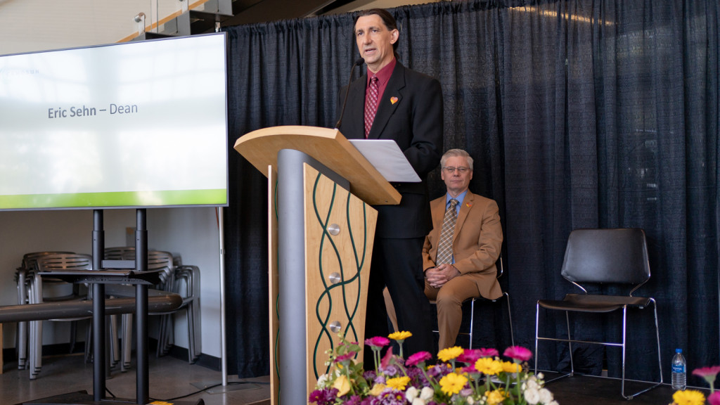 A man in a suit is standing at a podium speaking to a crowd at the awards ceremony. 