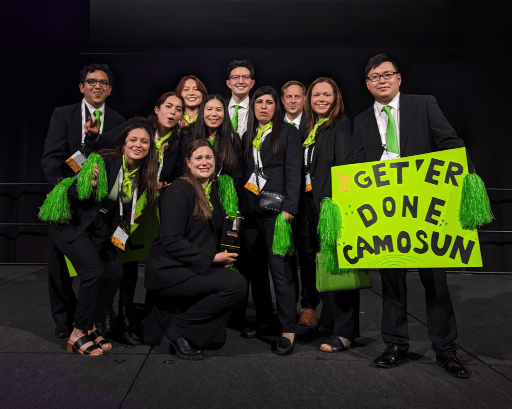 A group of students in suits celebrate on a stage, holding a sign that says 'Get'er done Camosun!'