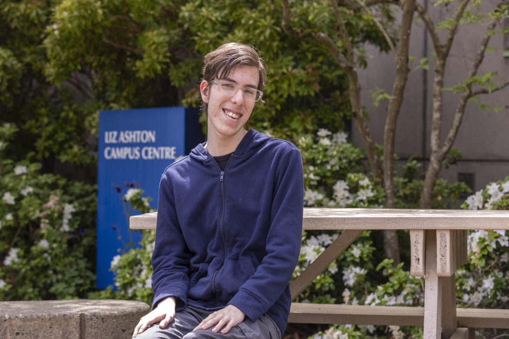 Caleb is sitting at the picnic tables in front of LACC. 