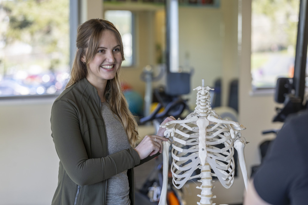 Sarah smiling, holding human skeleton model beside her. 
