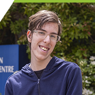 Kaleb sitting and smiling in front of the LACC building in the Interurban Campus.