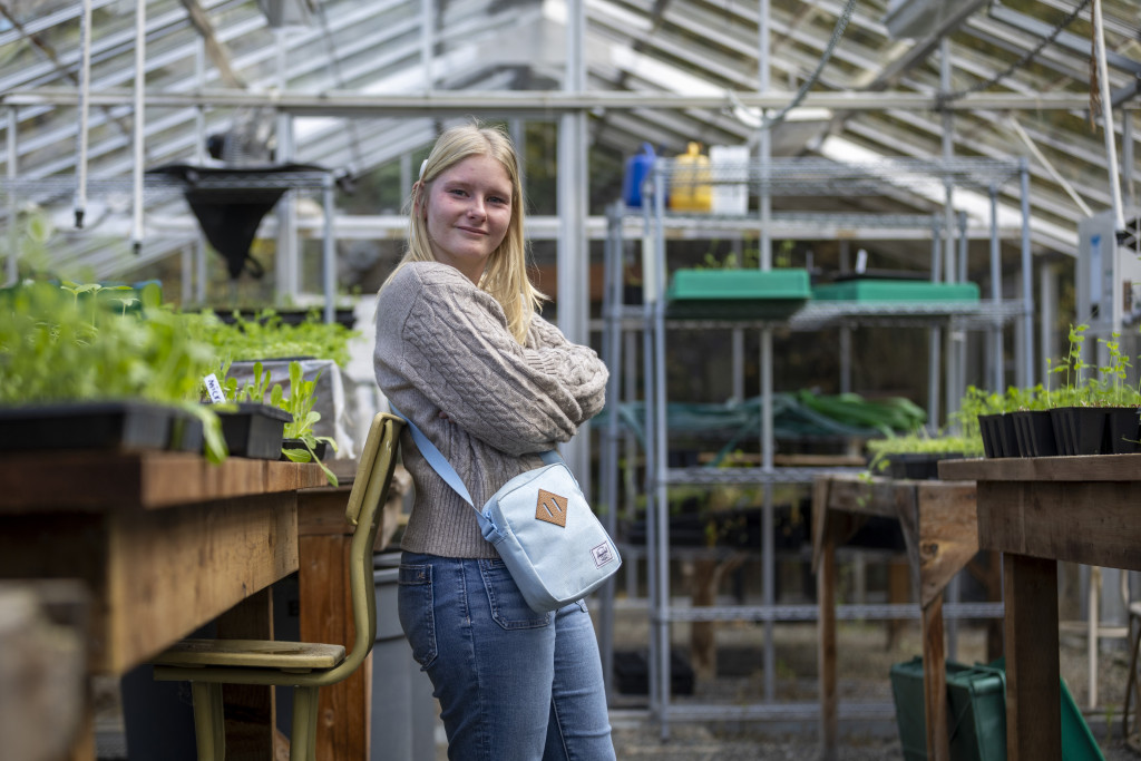 ETP student Kyla Kelly strikes a pose for the camera. Kyla is leaning against a wooden plant container inside a greenhouse.