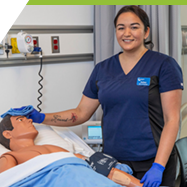 An Indigenous Health Care assistant student wipes the brow of a practice dummy in a hospital bed. 