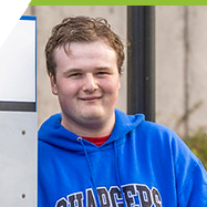 Jacob standing next to the Interurban Campus banner, wearing a blue Chargers hoodie.