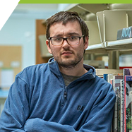 Nic standing by the bookshelf in the library