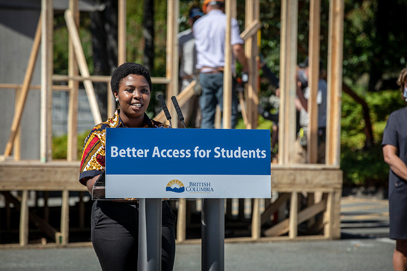 A young black woman gives a speech at a podium that has a Government of British Columbia sign that says "Better Access for Students"