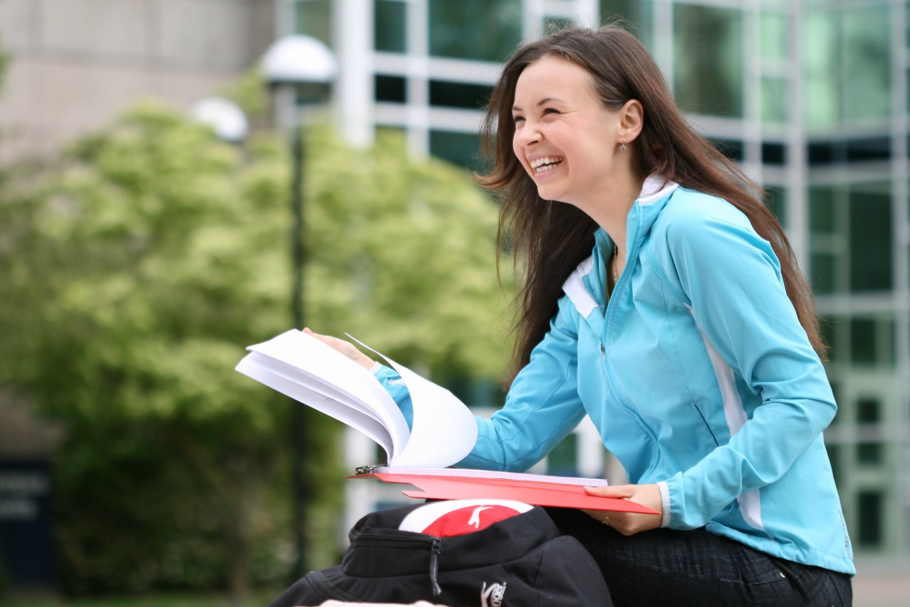 A student sits on a picnic table in the sun. She is laughing. 