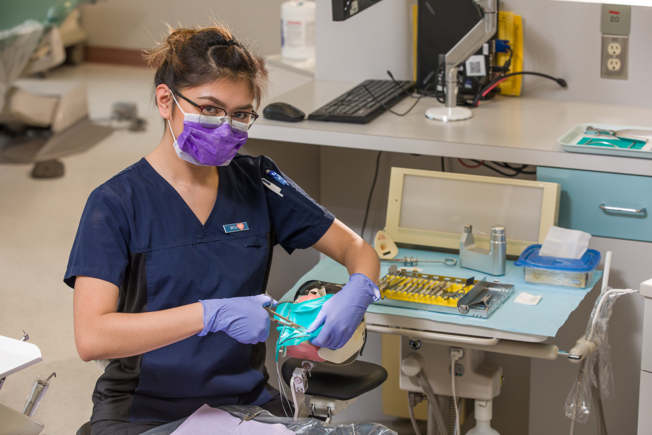 a dental student practices a procedure on a teaching mannequin in a dentist office