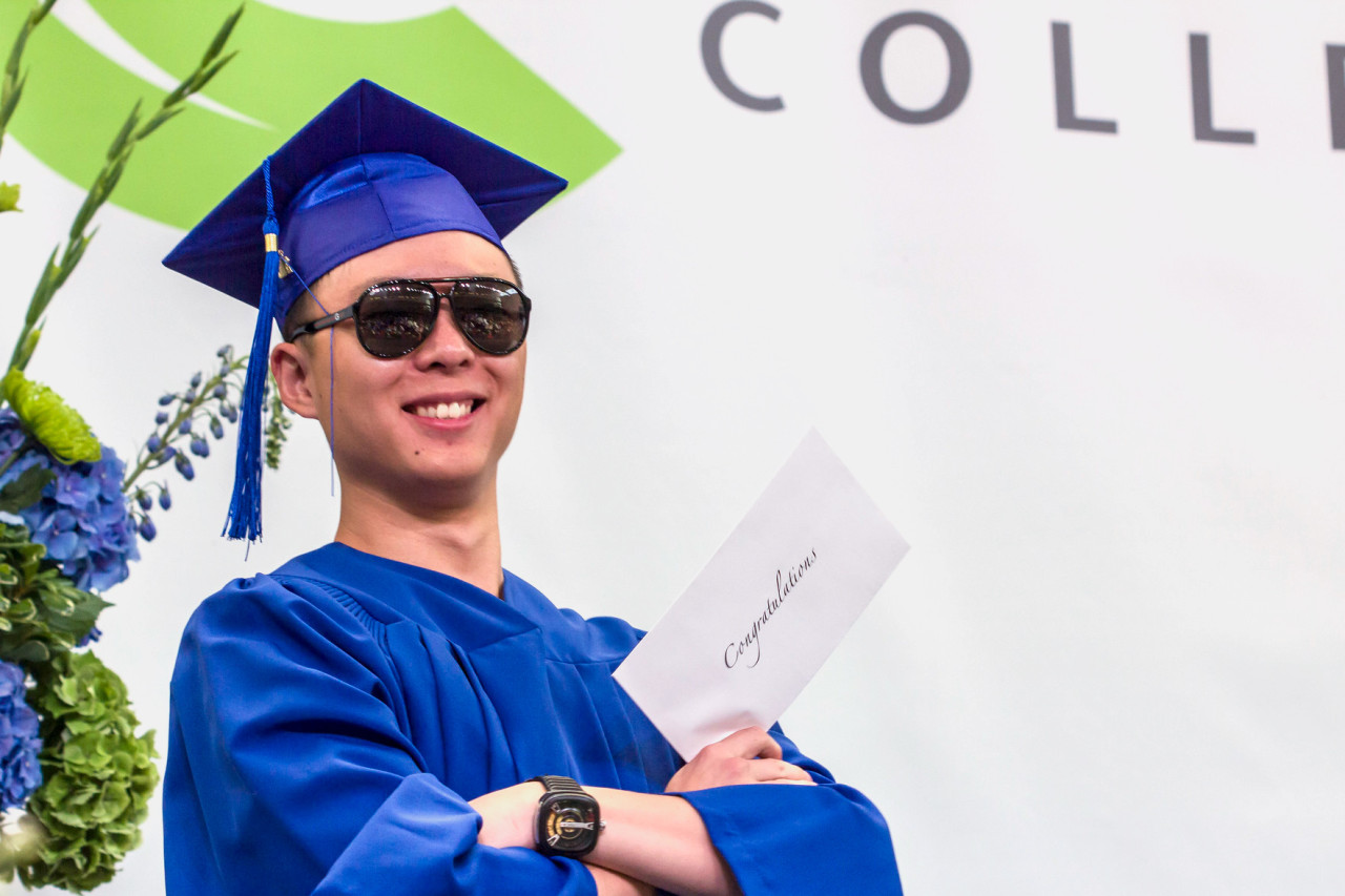 A young student in a graduation cap and gown proudly shows off his diploma