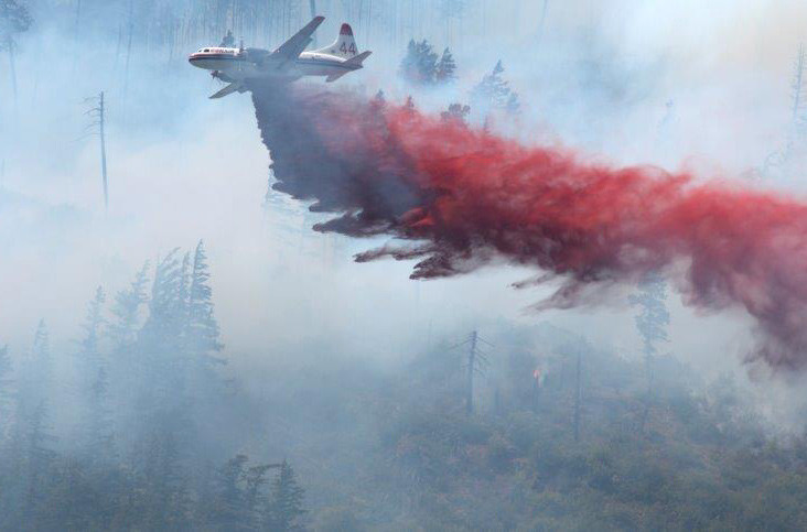 A Conair plane drops fire-retardant over an active wildfire area in Lytton, B.C.