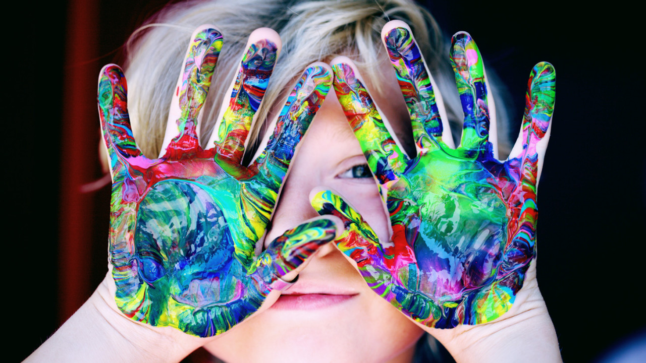 A child holds his hands up. They are covered in finger paint.