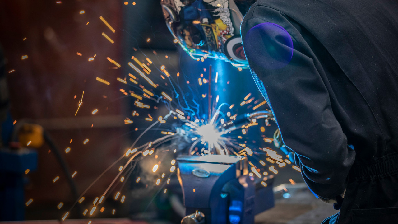 a student decked out in welding gear is working on a piece and covered in sparks 