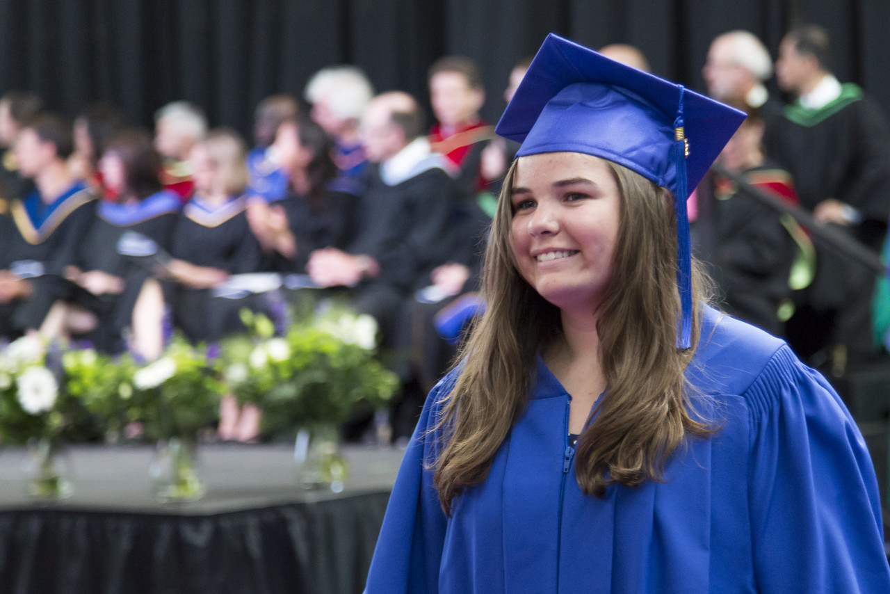 A happy student in a graduation gown walks off the stage with her diploma in hand 