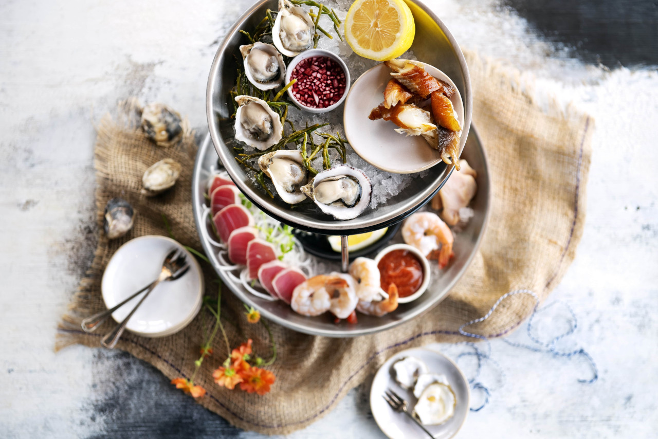 Oysters, prawns and sushi arranged in stacked serving plates against a light background
