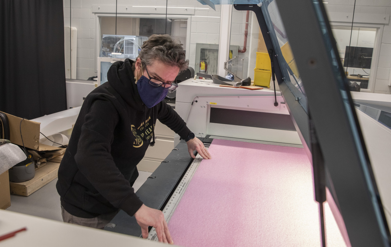 A man leans over a commercial laser cutter placing a sheet of foam