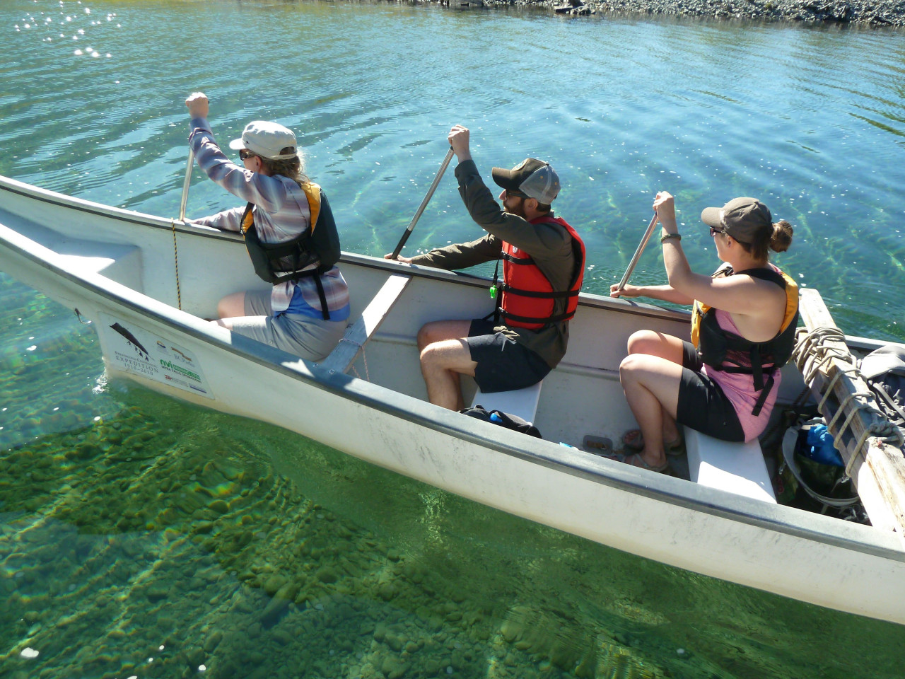 three adventure education students canoeing in the sunshine on crystal clear green water in strathcona park