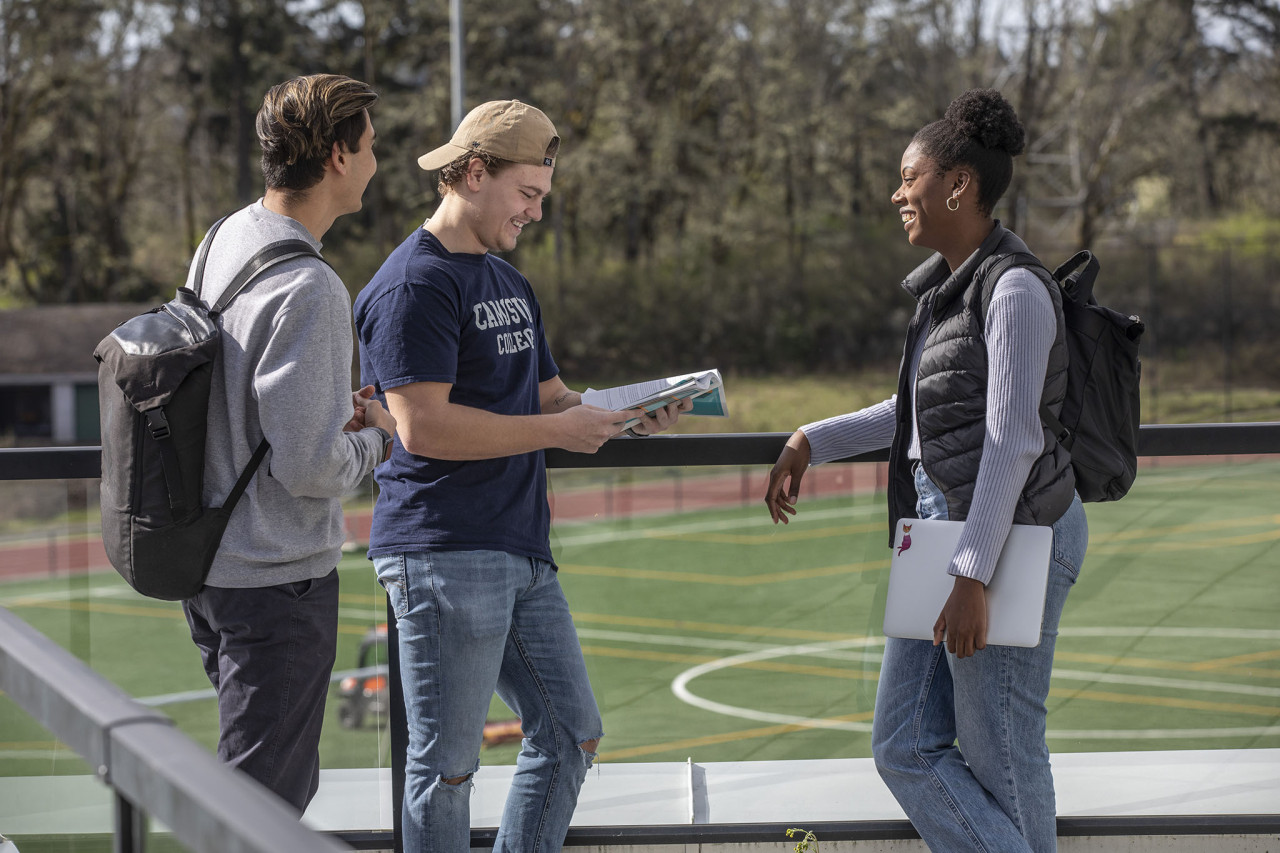three sport management students talking outside overlooking the track and field