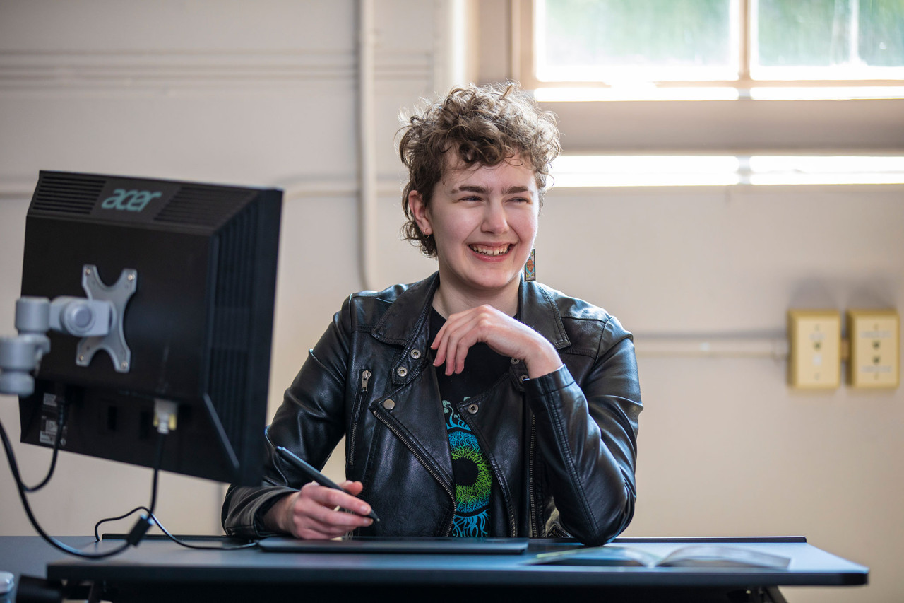 Comics and Graphic Novels student, Rhys, smiling while working in the computer lab.