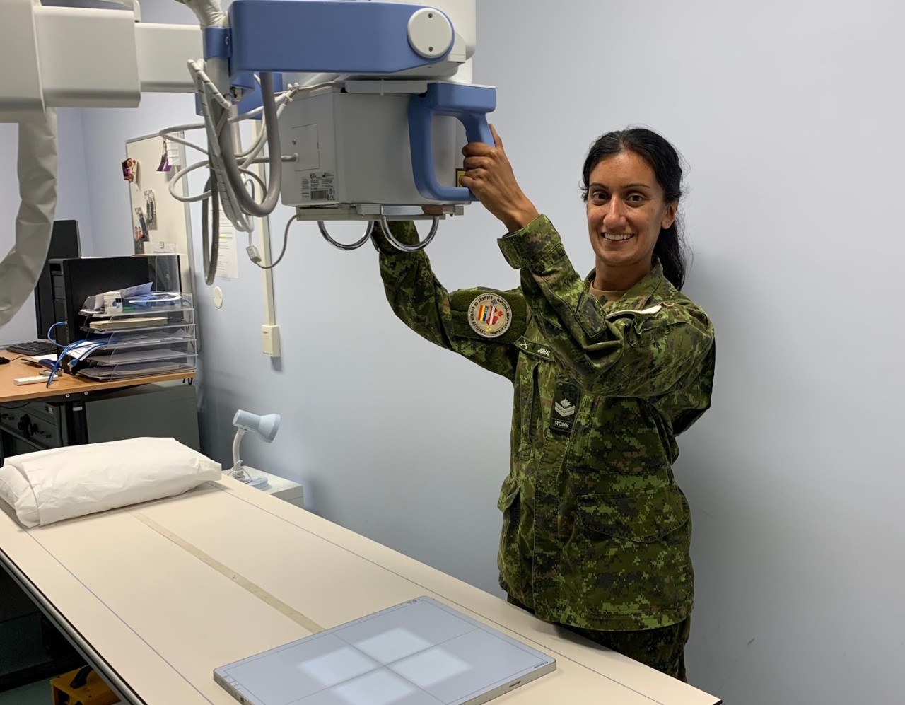 MRAD alumni dressed in military uniform poses with an overhead x-ray machine.