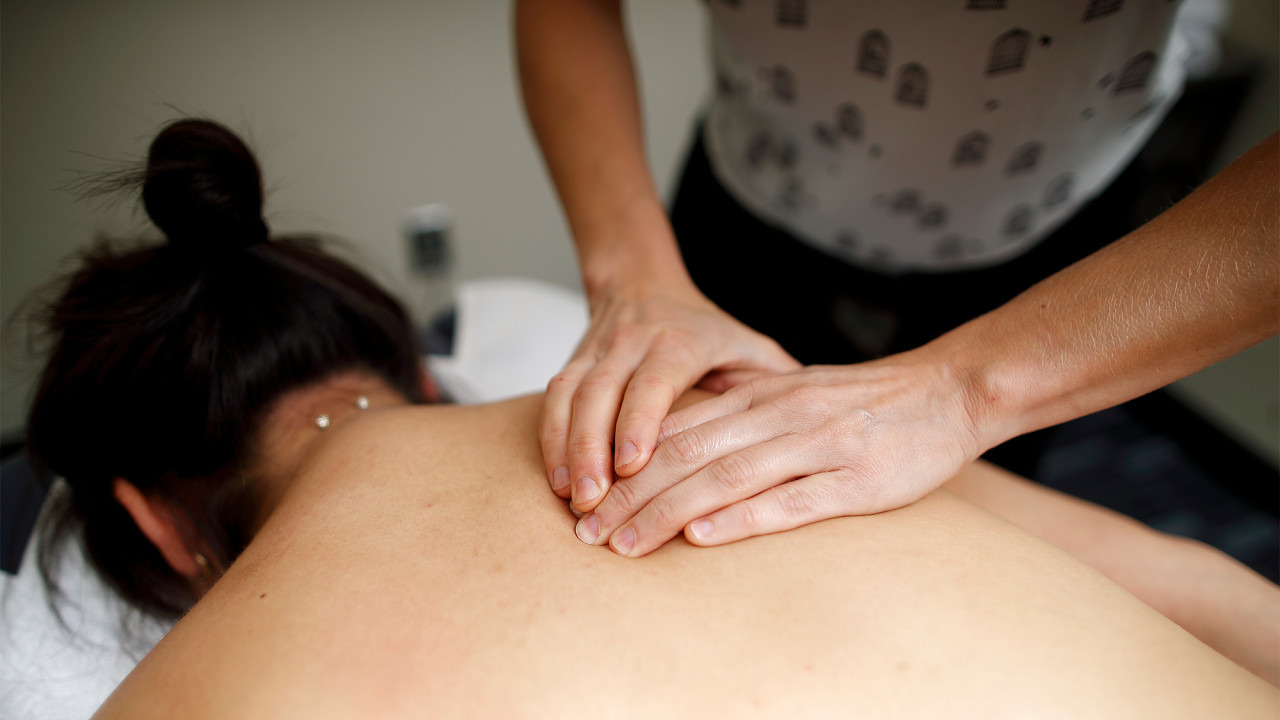 massage therapy instructor showing manual technique on student client to two student practitioners watching out of frame