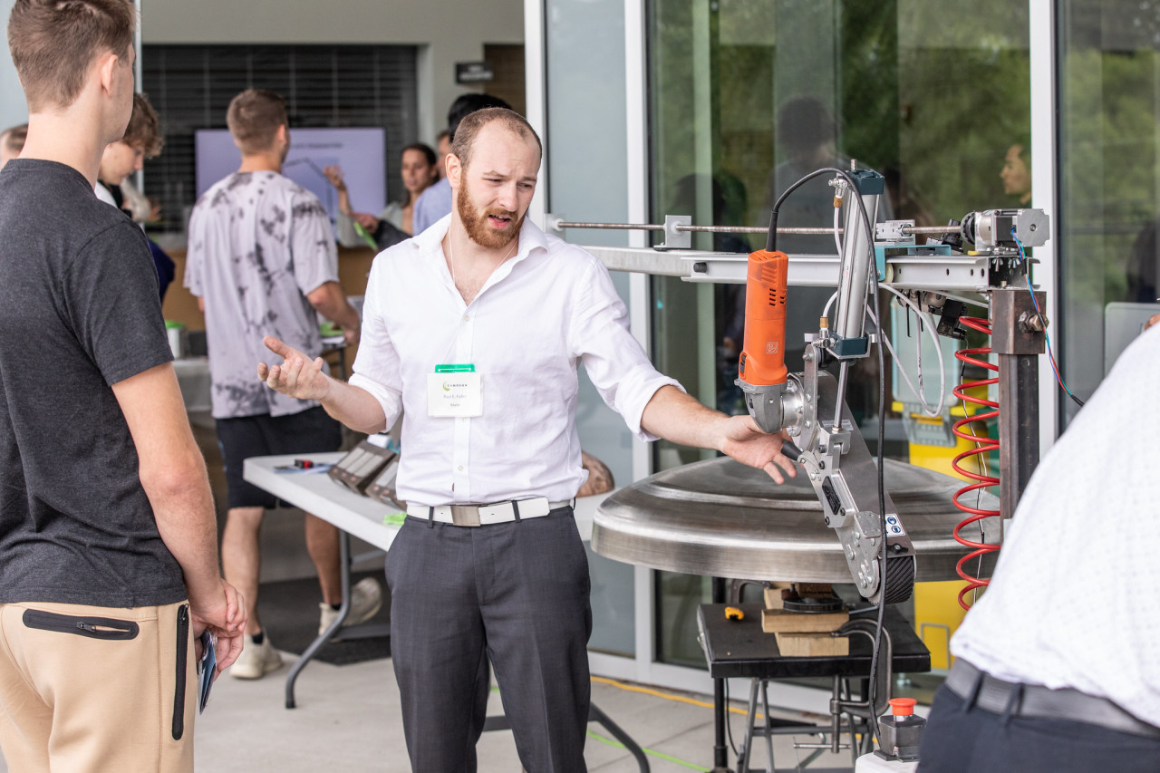 A mechanical engineering student explains his project to onlookers at a capstone event.