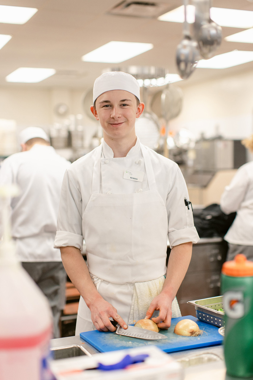 A culinary students practices chopping vegetables in the teaching kitchen.