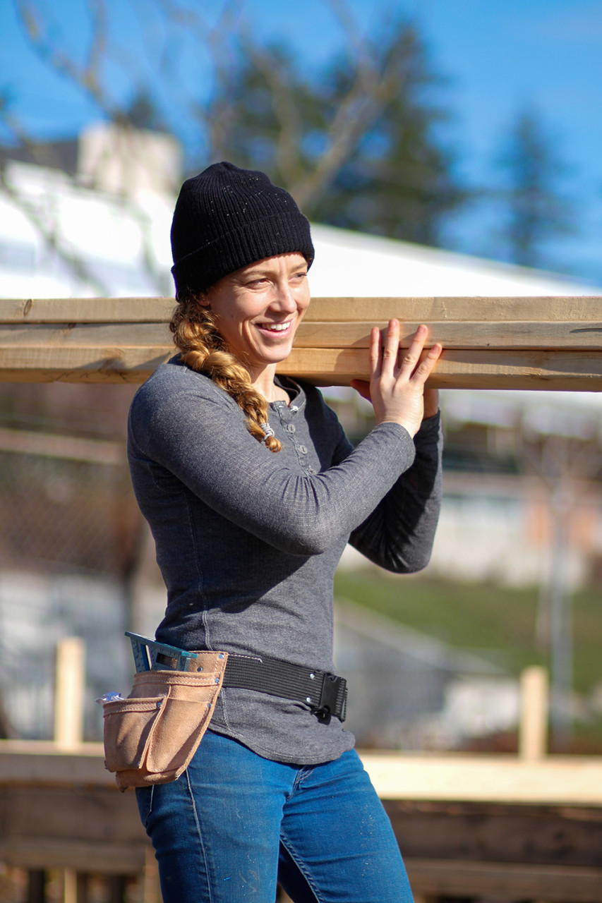 Female trades person carrying lumber on a construction jobsite. 