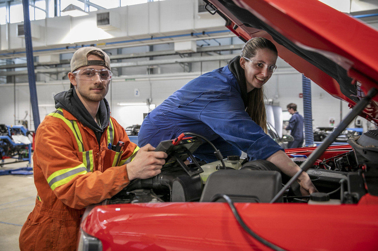 Two auto mechanics working under the hood of a truck diagnose engine trouble.